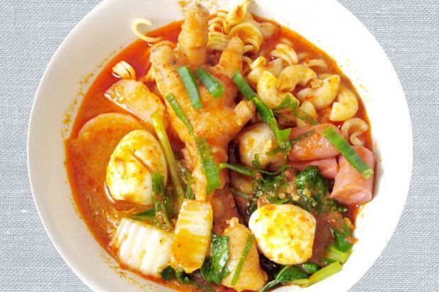 Seblak khas Bandung dengan tambahan ceker dan sosis, jajanan pedas yang menggugah selera.